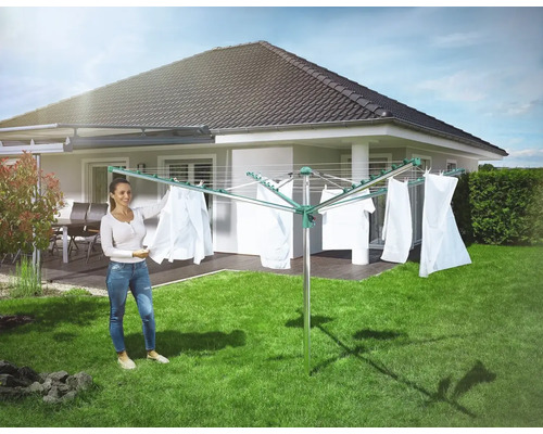 Frau hängt Wäsche auf eine Wäschespinne im Garten.