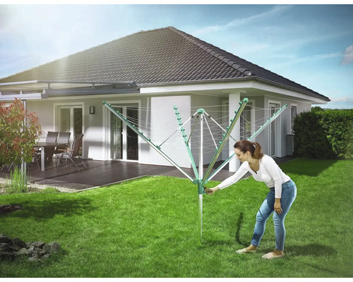 Frau bedient Wäschespinne im Garten vor Haus