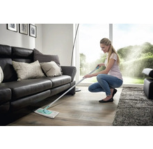 Frau wischt Holzboden im Wohnzimmer mit einem Bodenwischer.