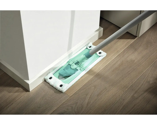 Serpillière avec housse en microfibres nettoyant un parquet contre un mur blanc.