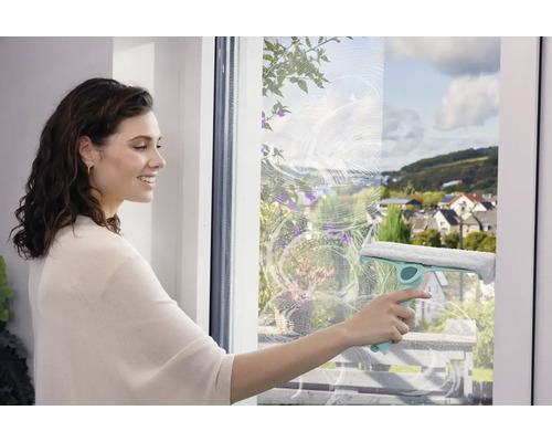 Frau putzt Fenster mit einem Fensterwischer für streifenfreie Sauberkeit