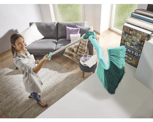 Une femme utilise une brosse avec un manche pour nettoyer le salon.