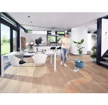 Femme nettoyant un parquet dans un salon lumineux avec un balai à franges et un seau