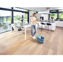 Femme nettoyant un plancher en bois avec une serpillère et un seau dans un espace de vie lumineux.