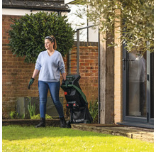 Une femme se tient avec un broyeur de végétaux dans le jardin.