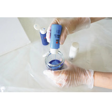 Eine Person mischt blaue Giessharzfarbe in einem Glasbehälter für Kunstprojekte.