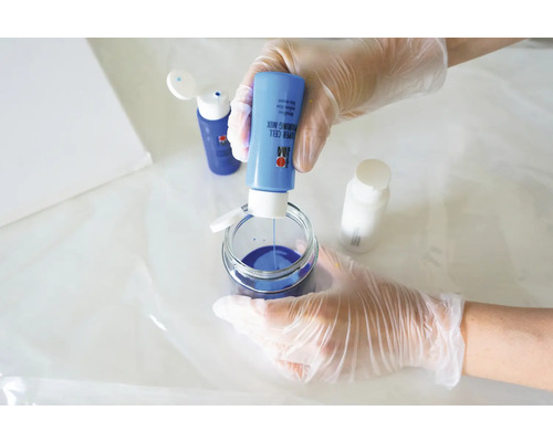 Eine Person mischt blaue Giessharzfarbe in einem Glasbehälter für Kunstprojekte.