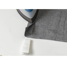 Un fer à repasser sur un tissu gris avec du ruban thermocollant.