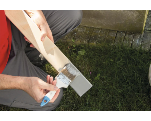 Eine Person streicht ein Holzbrett mit einem Pinsel.