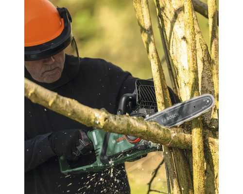 Une personne coupe des branches avec une tronçonneuse à batterie Bosch, tout en portant des lunettes de protection et un casque.