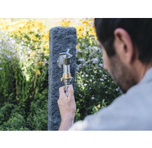Gartenszene mit Wasserhahn an Steinsäule und Person, die einen Schlauch anschliesst