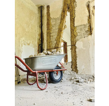 Une brouette remplie de gravats devant un mur partiellement démoli.