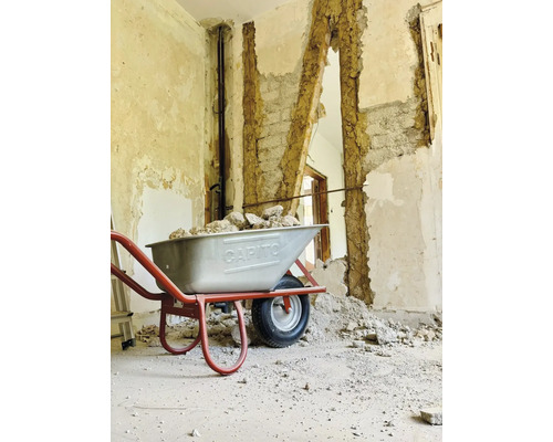 Une brouette remplie de gravats devant un mur partiellement démoli.