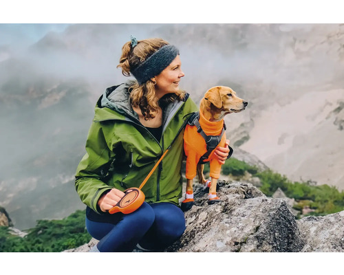 Frau mit Hund auf einem Berg, der Hund trägt einen Overall und Schuhe