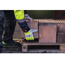 Une personne en vêtements de travail et gants de travail soulève une brique d'une palette en bois.
