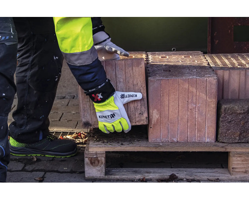 Une personne en vêtements de travail et gants de travail soulève une brique d'une palette en bois.