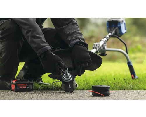 Une personne remplace la lame d'un coupe-bordure, avec une batterie et une bobine à proximité.