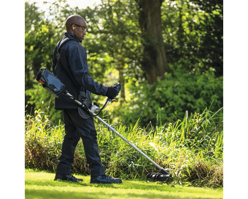 Homme coupant l'herbe avec un coupe-bordures sans fil dans le jardin.