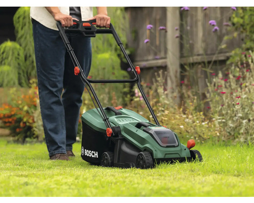 Une personne utilise une tondeuse à gazon Bosch verte sur une pelouse.