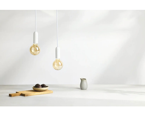 Zwei Pendelleuchten mit Glühbirnen hängen über einem Holztisch mit Schüssel und Krug.