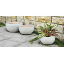 Drei runde Pflanzgefäße im Aussenbereich vor einer Steinmauer.