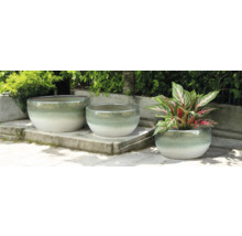 Drei runde Pflanzgefäße aus Keramik auf einer Steinterrasse, eines davon mit einer Pflanze.
