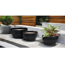 Trois pots de fleurs noirs de différentes tailles sur une marche en pierre avec des plantes