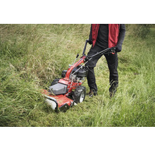 Person bedient eine Motorhacke im hohen Gras.