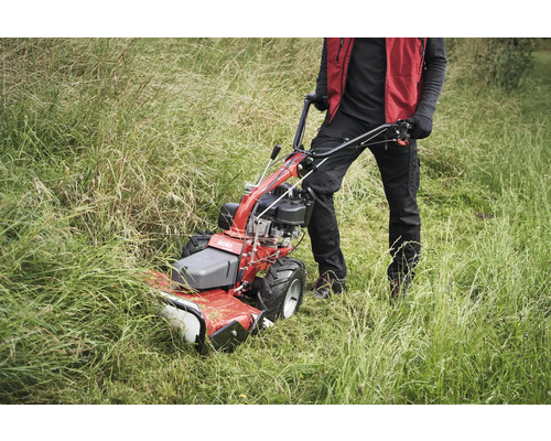 Person bedient eine Motorhacke im hohen Gras.