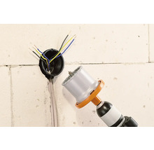 Bohrmaschine mit Bohrkrone neben einer Wandsteckdose mit Kabeln