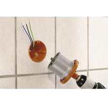 Une perceuse avec une scie cloche perce un trou dans un mur carrelé pour une prise électrique.