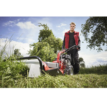 Un homme utilise une faucheuse à fléaux Solo rouge dans un pré.
