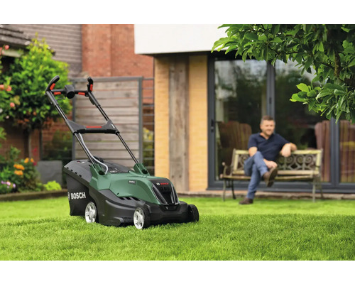 Bosch Rasenmäher auf Rasenfläche mit sitzendem Mann im Hintergrund