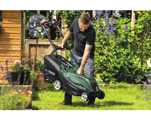 Mann hebt Rasenmäher im Garten an