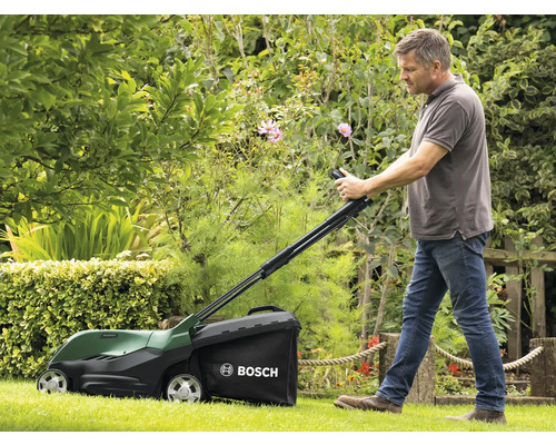 Un homme utilise une tondeuse à gazon Bosch dans un jardin.