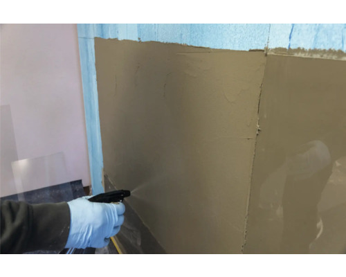 Une personne humidifie un mur avec un vaporisateur sur lequel de l'enduit a déjà été appliqué.