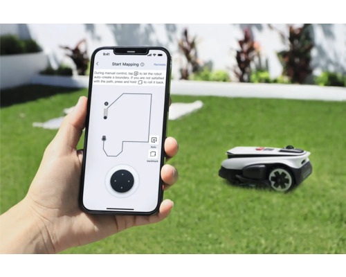 Une personne tient un smartphone avec une application pour contrôler un robot tondeuse dans le jardin.