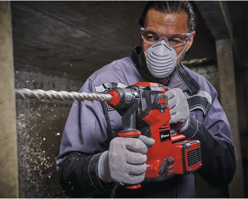 Mann bohrt mit einem Einhell Bohrhammer in eine Wand, wobei er Schutzbrille und Atemschutzmaske trägt