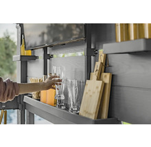 Une personne saisit un verre à bière dans un espace cuisine extérieure avec des étagères, des boissons, des verres, des planches à découper et une télévision.