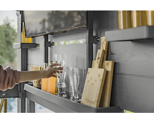 Une personne saisit un verre à bière dans un espace cuisine extérieure avec des étagères, des boissons, des verres, des planches à découper et une télévision.