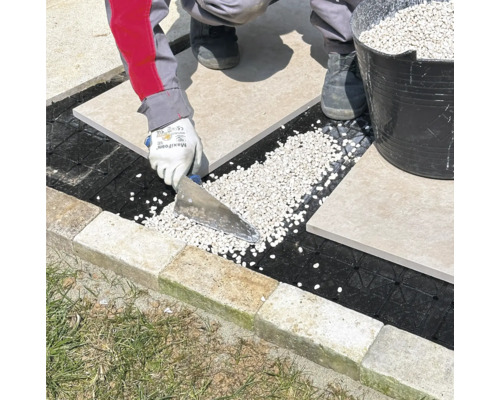 Pose de dalles de terrasse sur un lit de gravier à l'aide d'une spatule.