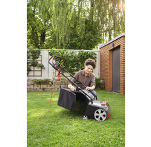 Eine Frau bereitet einen Rasenmäher mit Fangkorb für die Gartenarbeit vor.