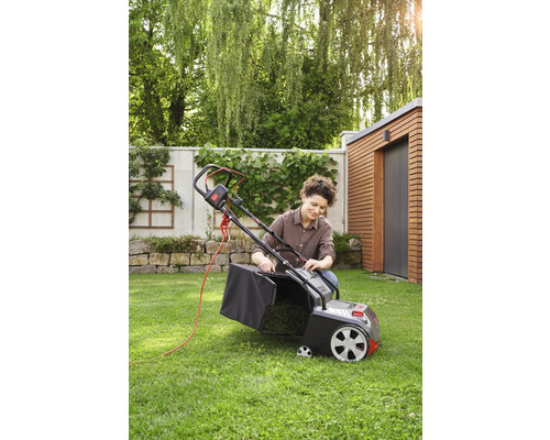 Eine Frau bereitet einen Rasenmäher mit Fangkorb für die Gartenarbeit vor.