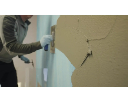 Une personne lisse du plâtre sur un mur à l'aide d'une truelle.