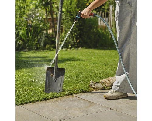Scène de jardin avec une personne nettoyant une bêche avec un tuyau d'arrosage