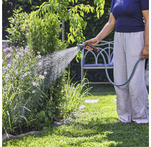 Une personne arrose des plantes dans le jardin avec un tuyau d'arrosage.