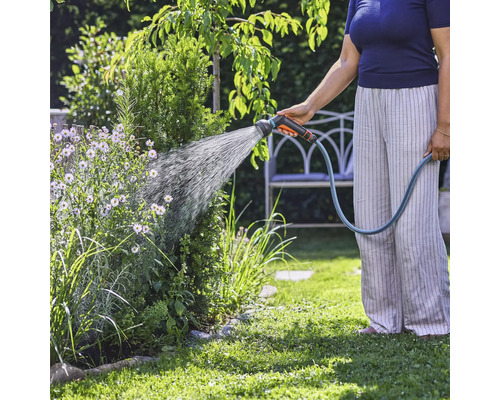 Une personne arrose des plantes dans le jardin avec un tuyau d'arrosage.