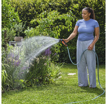 Une femme arrose des plantes de jardin avec un tuyau d'arrosage et un pistolet d'arrosage.
