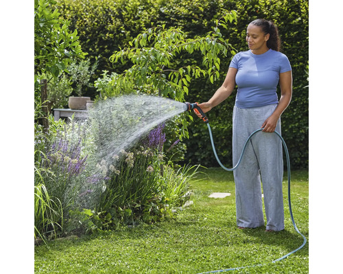 Une femme arrose des plantes de jardin avec un tuyau d'arrosage et un pistolet d'arrosage.