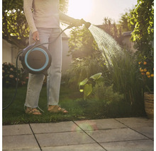 Frau giesst Pflanzen mit Schlauchaufroller im Garten.